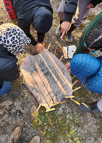 People stretch seal skin on the tundra.